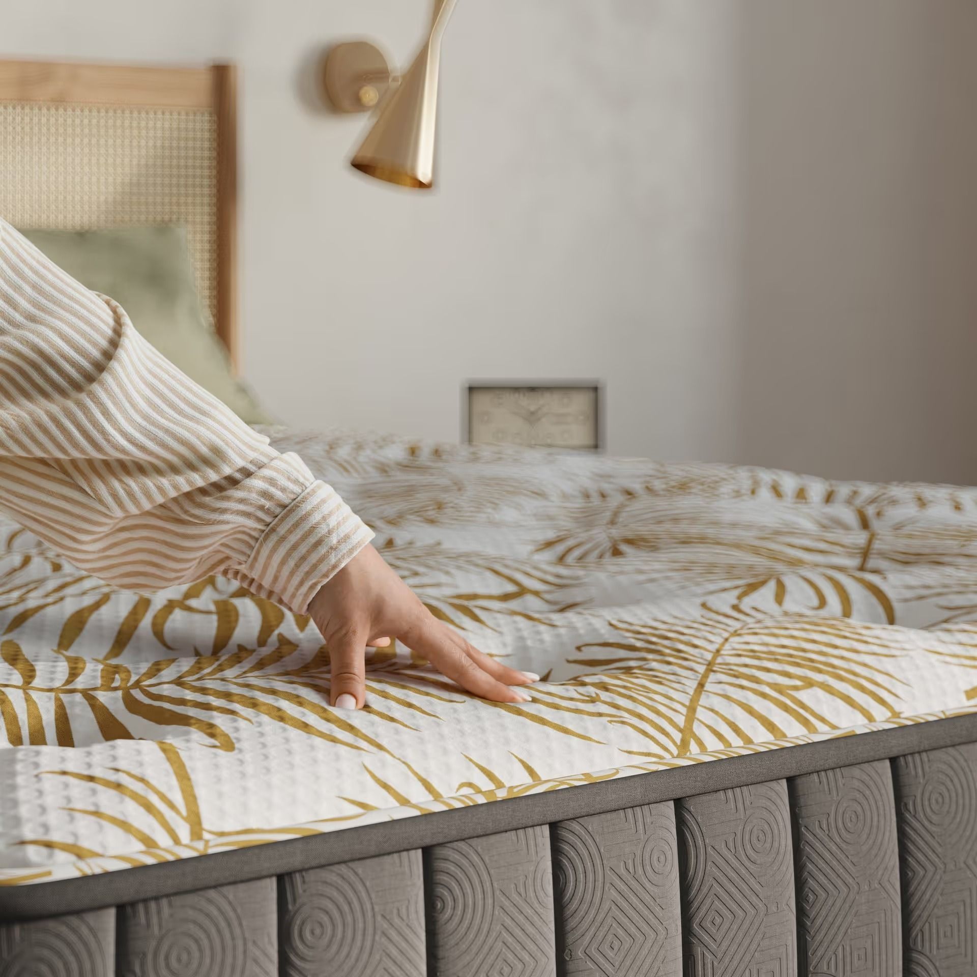 Product render showing a hand pressing into an upholstered mattress surface to demonstrate softness