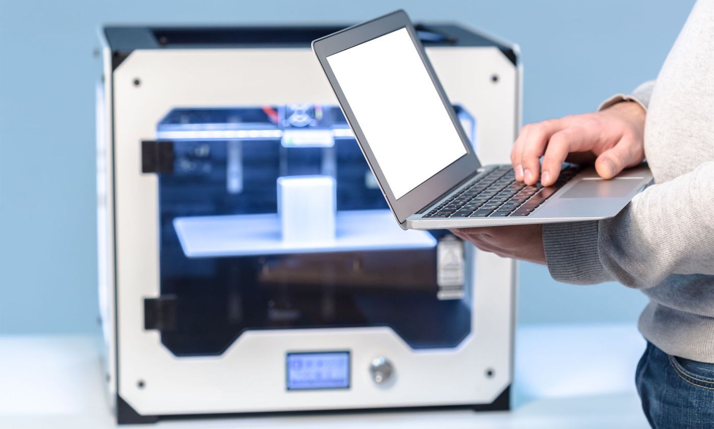 3D Printer and a man typing on laptop 