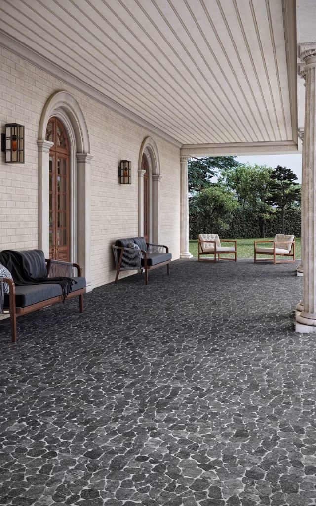3D render of a columned porch floored in black Cobbles Tumbled marble, with outdoor sofas along a cream brick wall