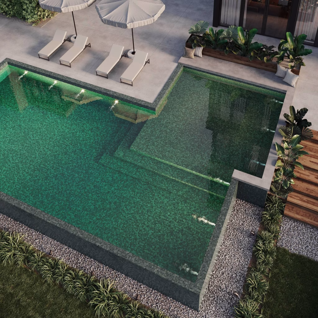 Aerial evening render of an L-shaped pool in dark green mosaic, with underwater lights and loungers on the deck