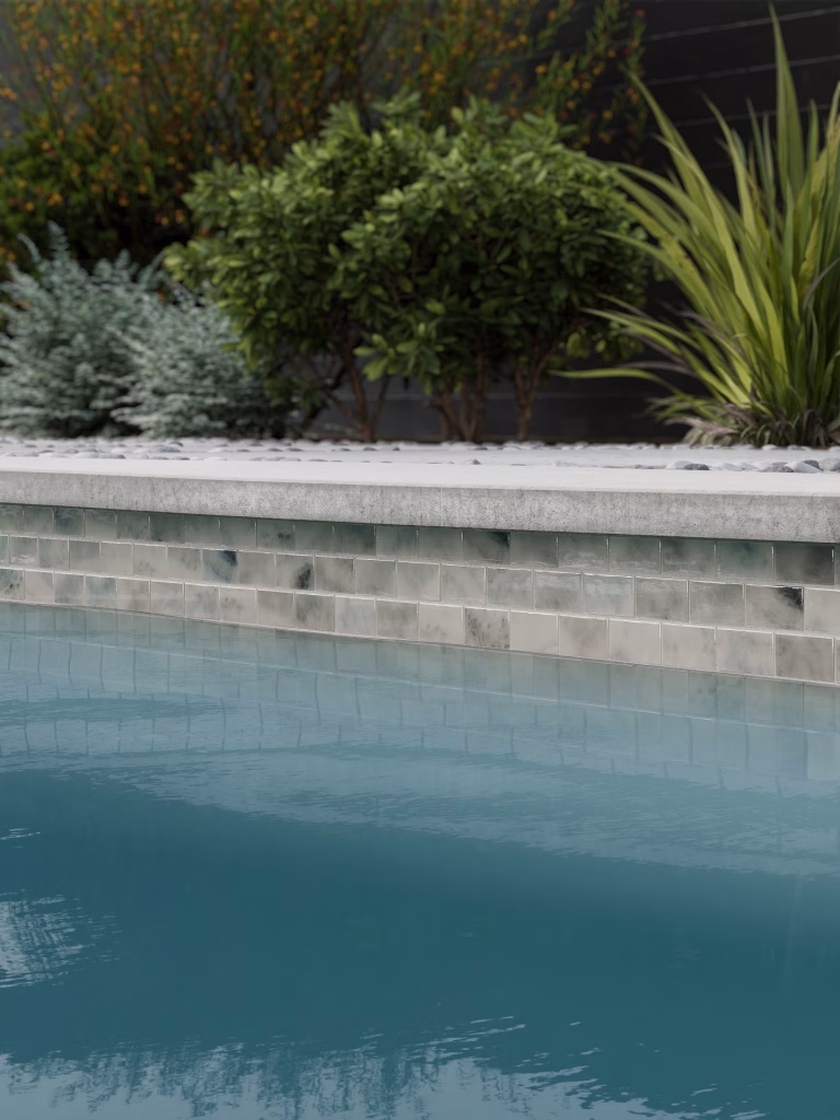 CGI close-up of a waterline band of pale grey-green glass tile under concrete coping, above calm blue pool water