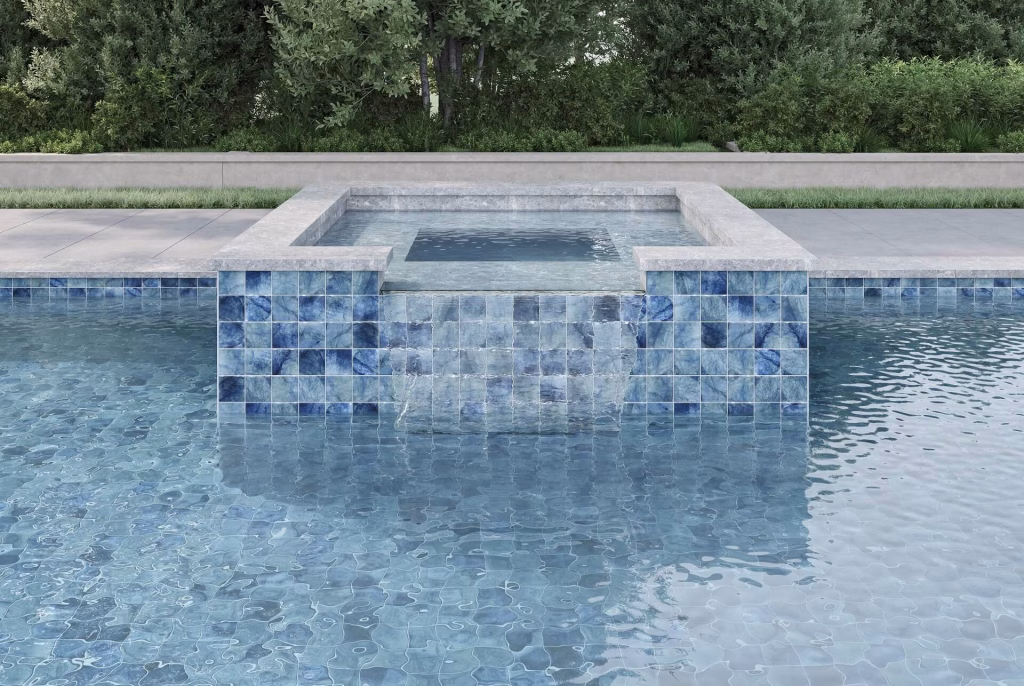 Raised spa with a sheet waterfall spilling into a pool, clad in blue veined tile that continues along the waterline and under the water