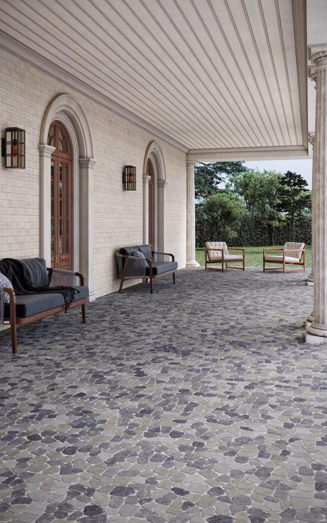 Render of a columned porch floored in grey and blue flat stone mosaic, with outdoor sofas along a cream brick-look wall