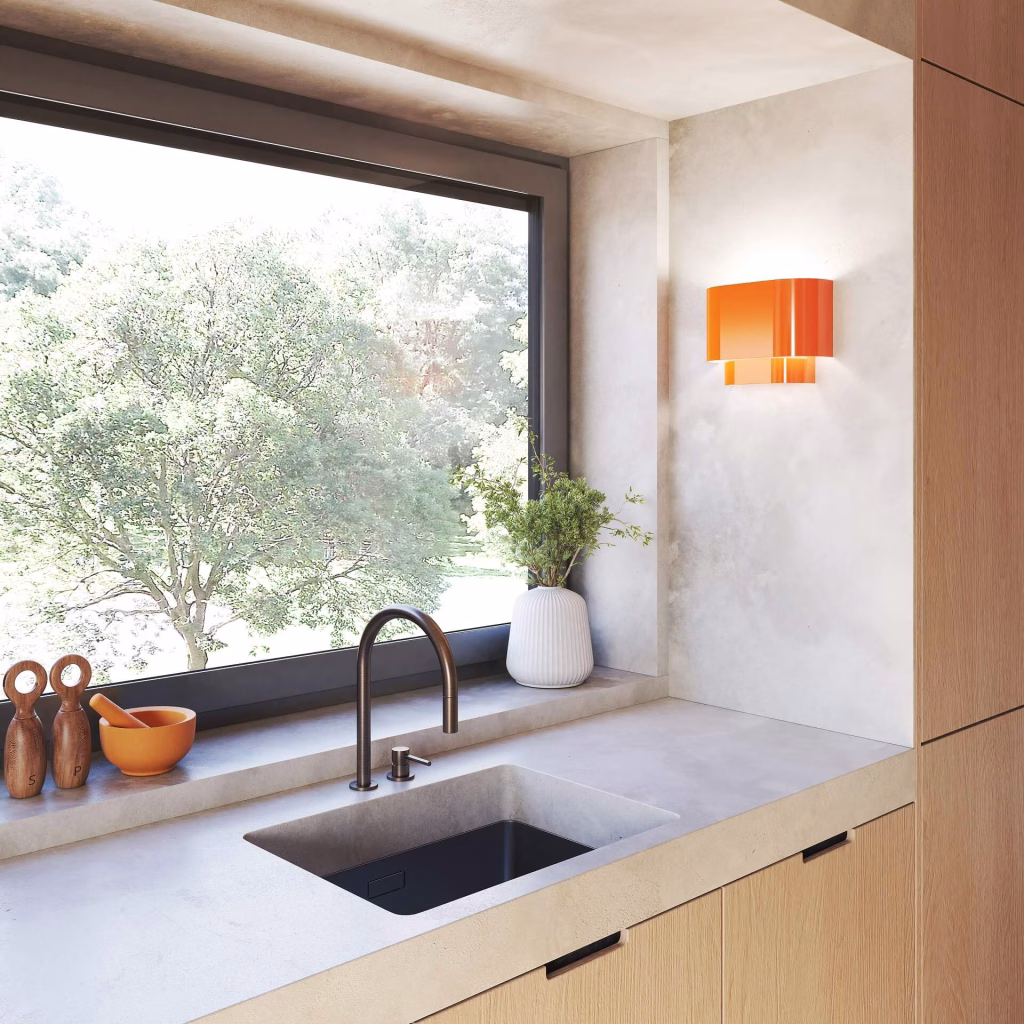 3D rendering of a glossy orange Livex Springview wall sconce above a concrete kitchen counter next to a garden window